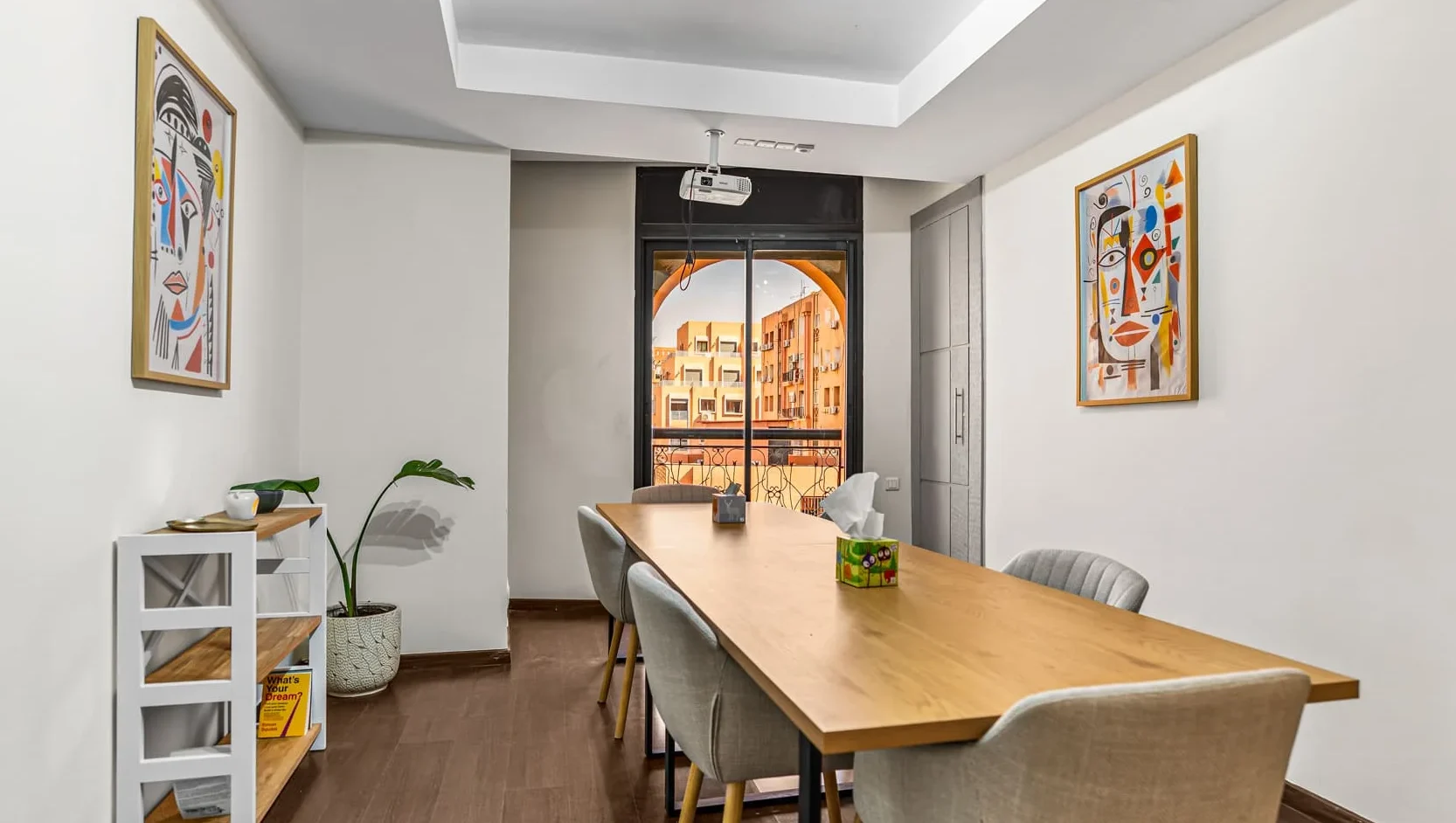 Meeting room at Qafila Society with a wooden table, grey chairs, a ceiling projector and an arched window view over Marrakech